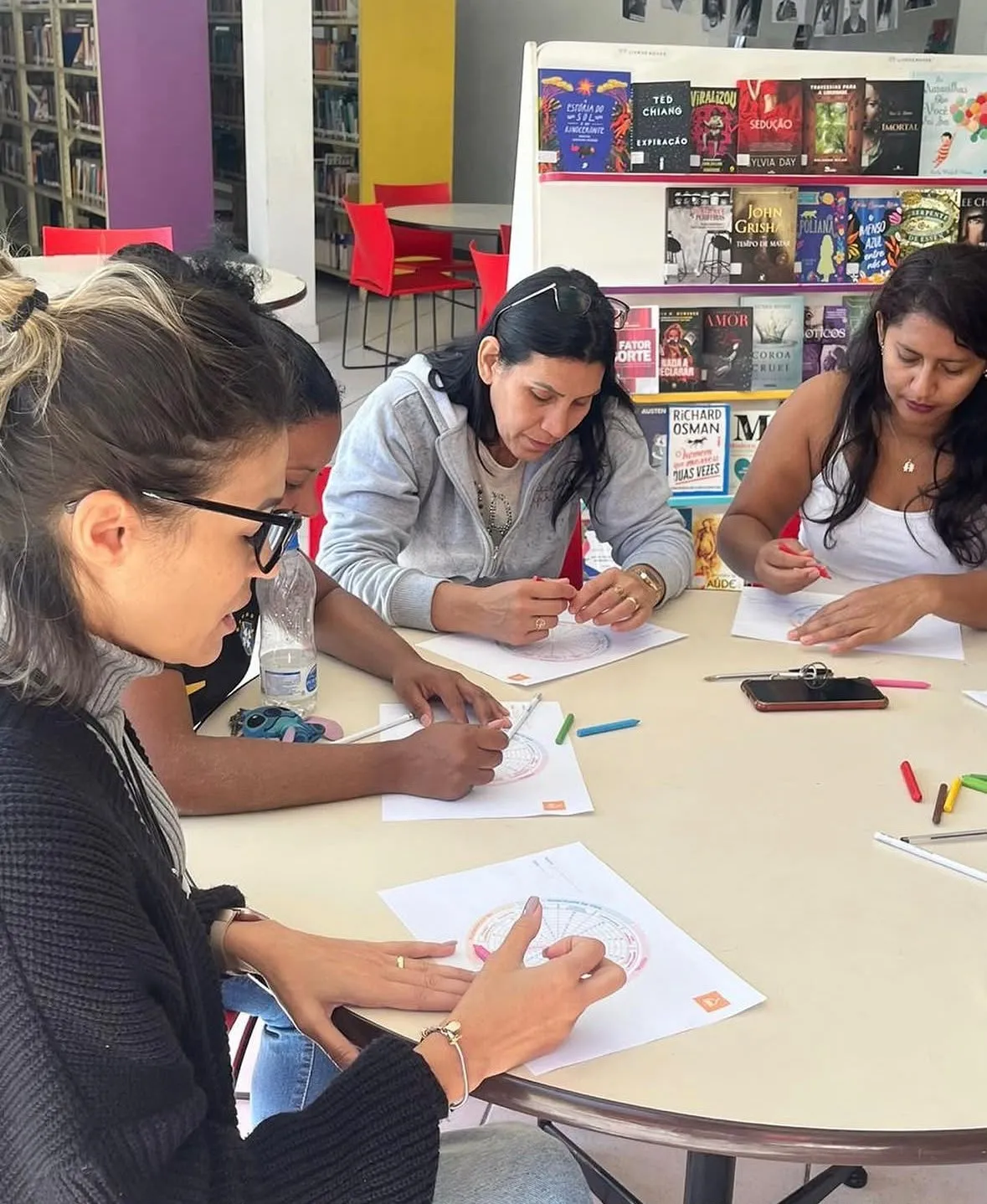 Participantes de um grupo terapêutico sentadas em volta de uma mesa, desenhando e colorindo